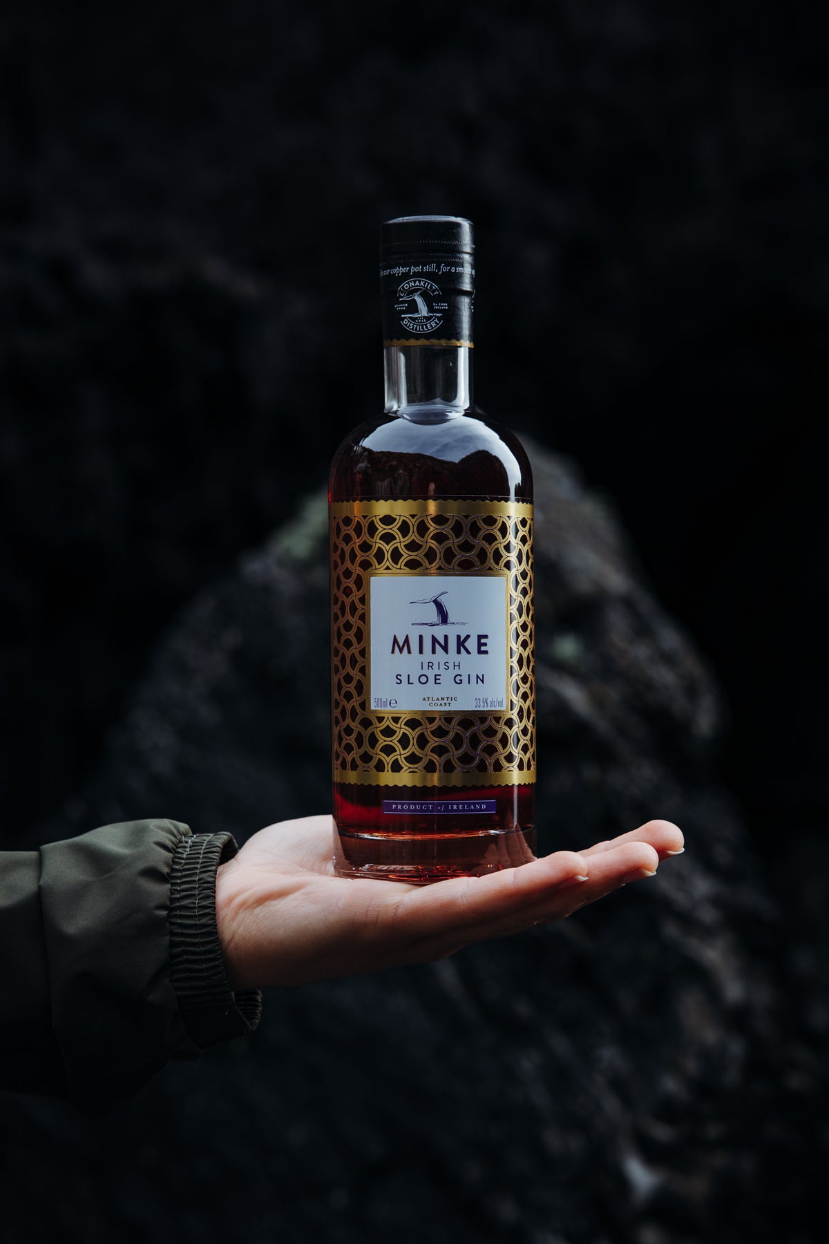 Minke Sloe Gin bottle held in hand against dark rock