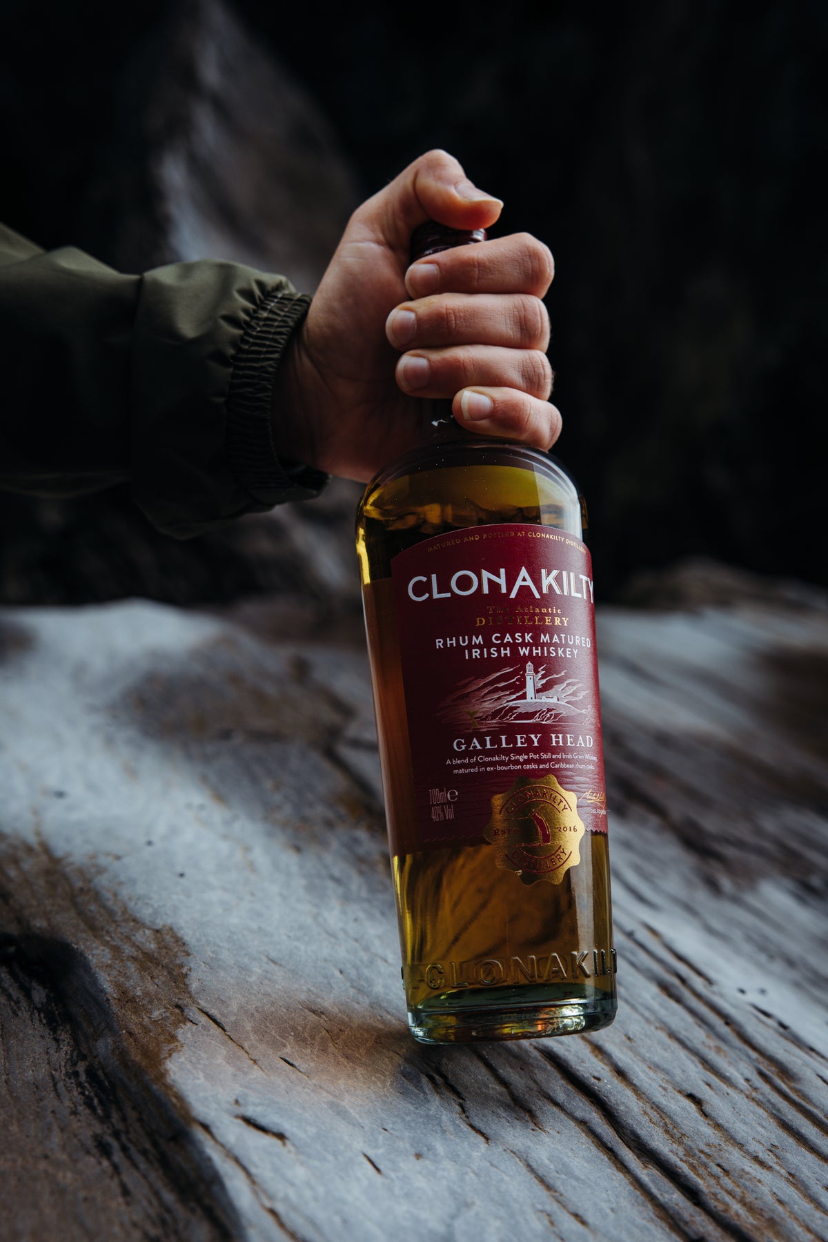 Clonakilty Galley Head Rhum Cask Irish Whiskey bottle held on weathered wood
